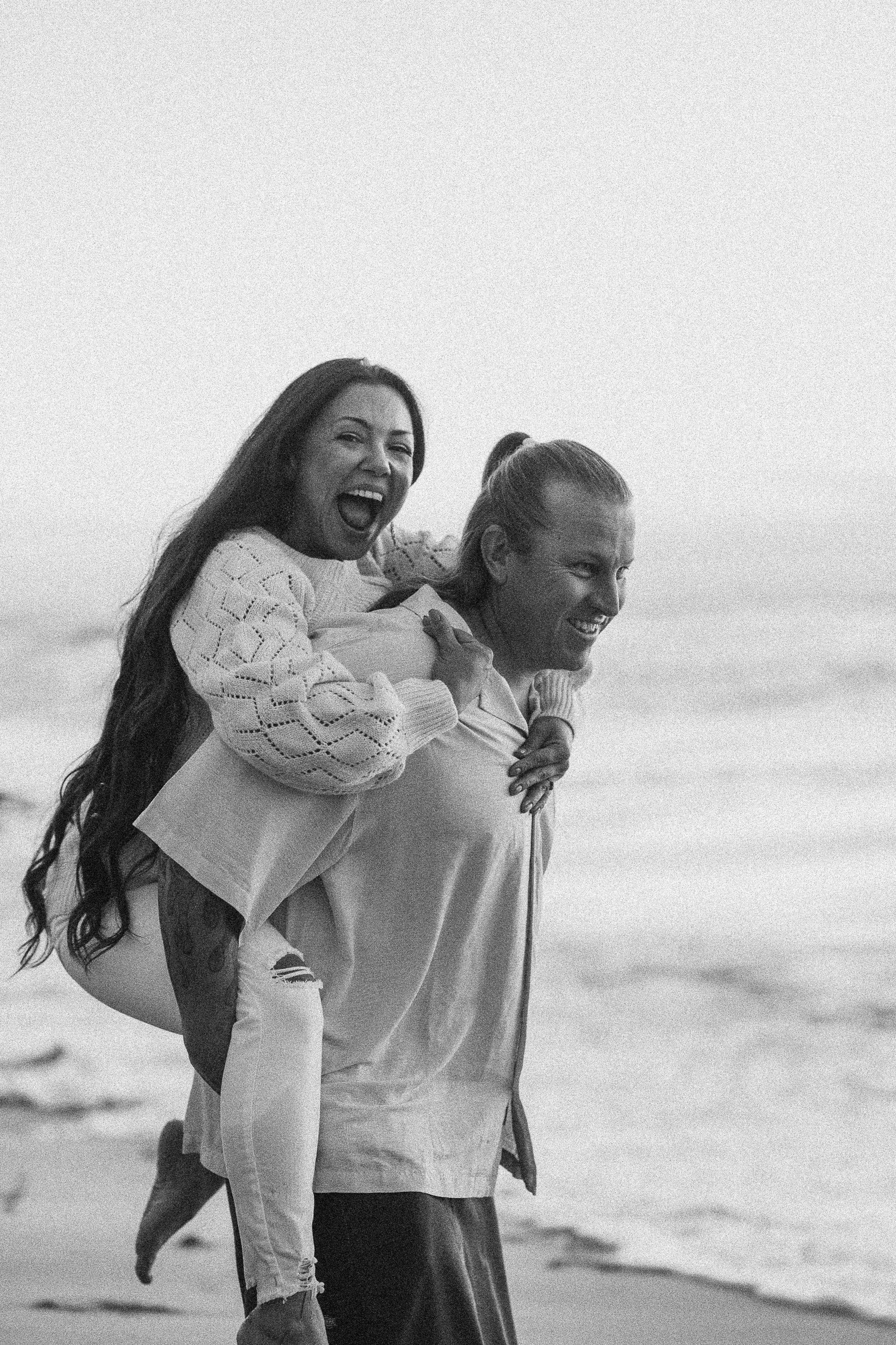A playful beach photoshoot with one person giving another a piggyback ride.