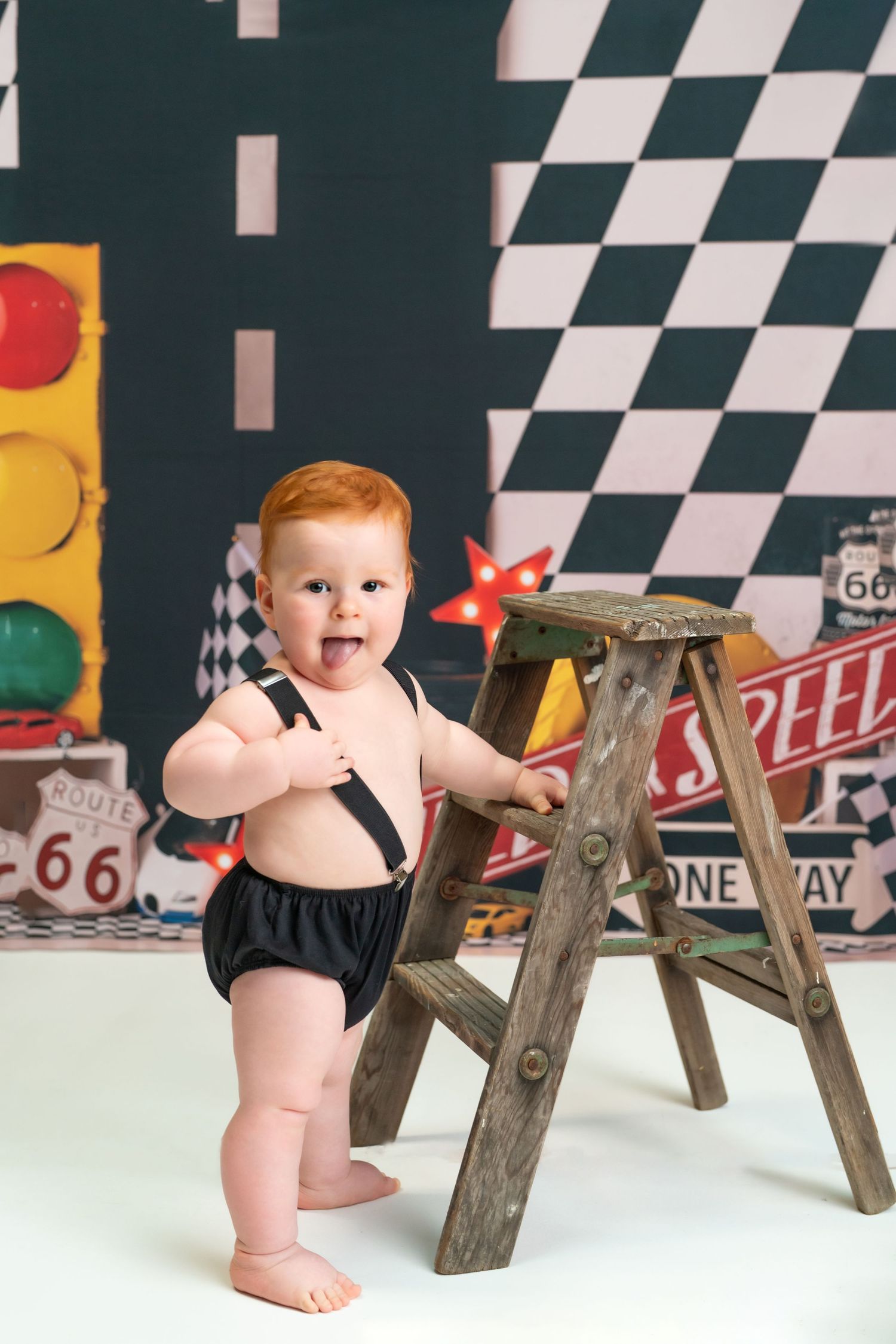 Baby in black outfit crawling near wooden benches against racing-themed backdrop with vintage signs.