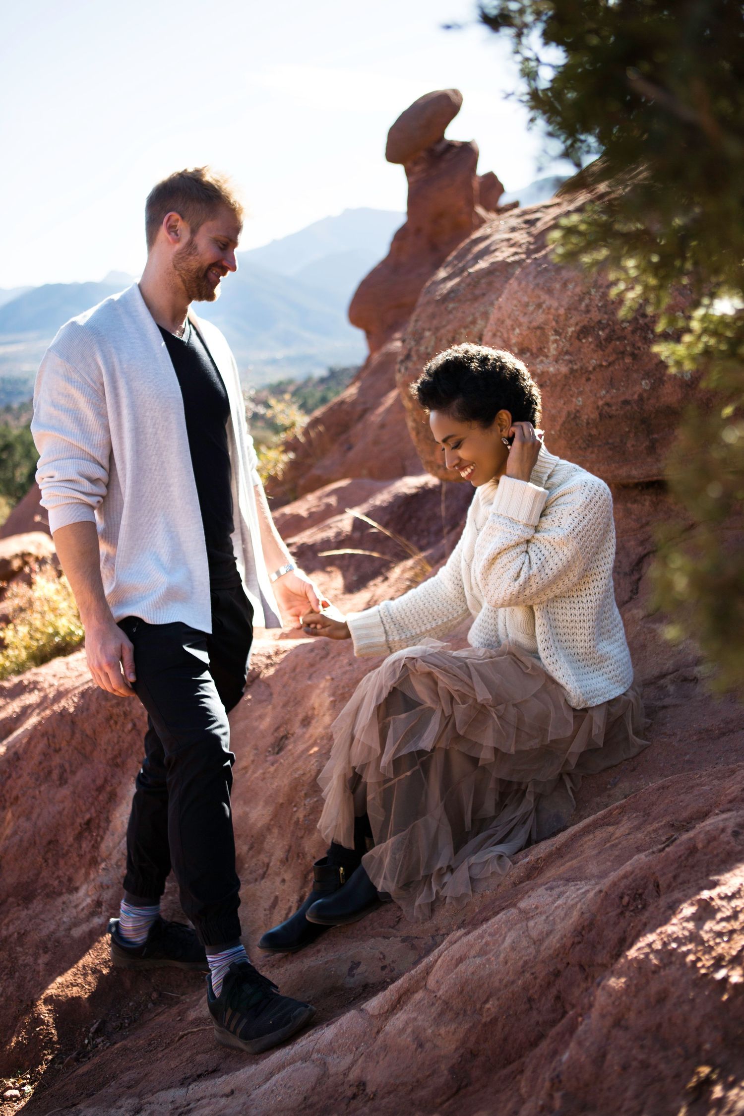 Couple sitting on red rocks during mountain engagement photoshoot.