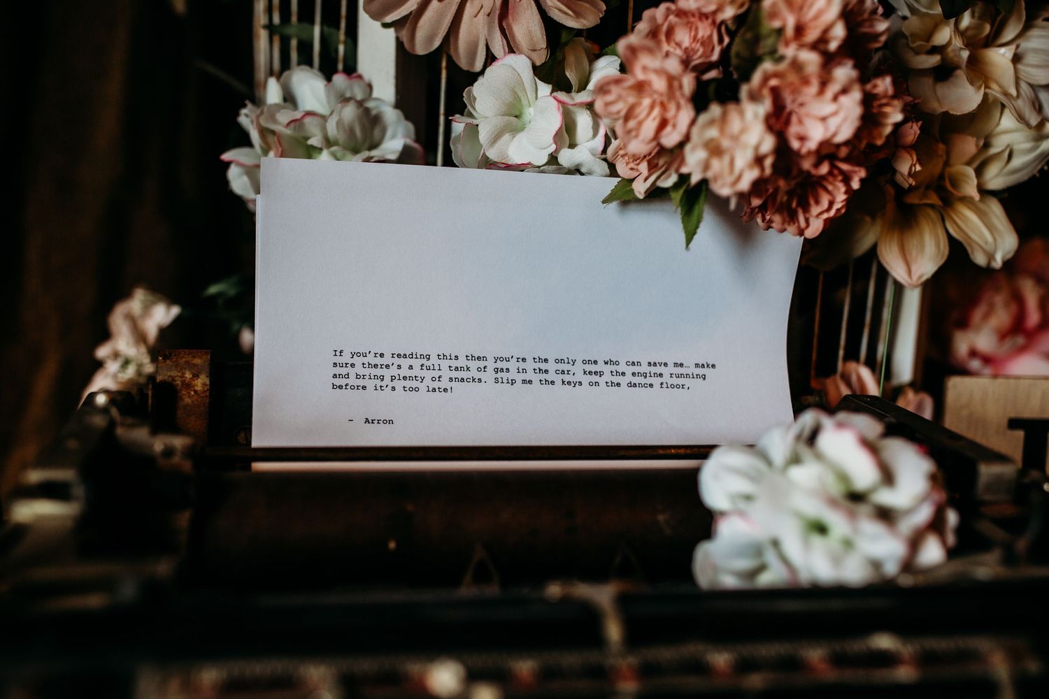 A typed message on white paper surrounded by soft pink and white flowers in a vintage setting.