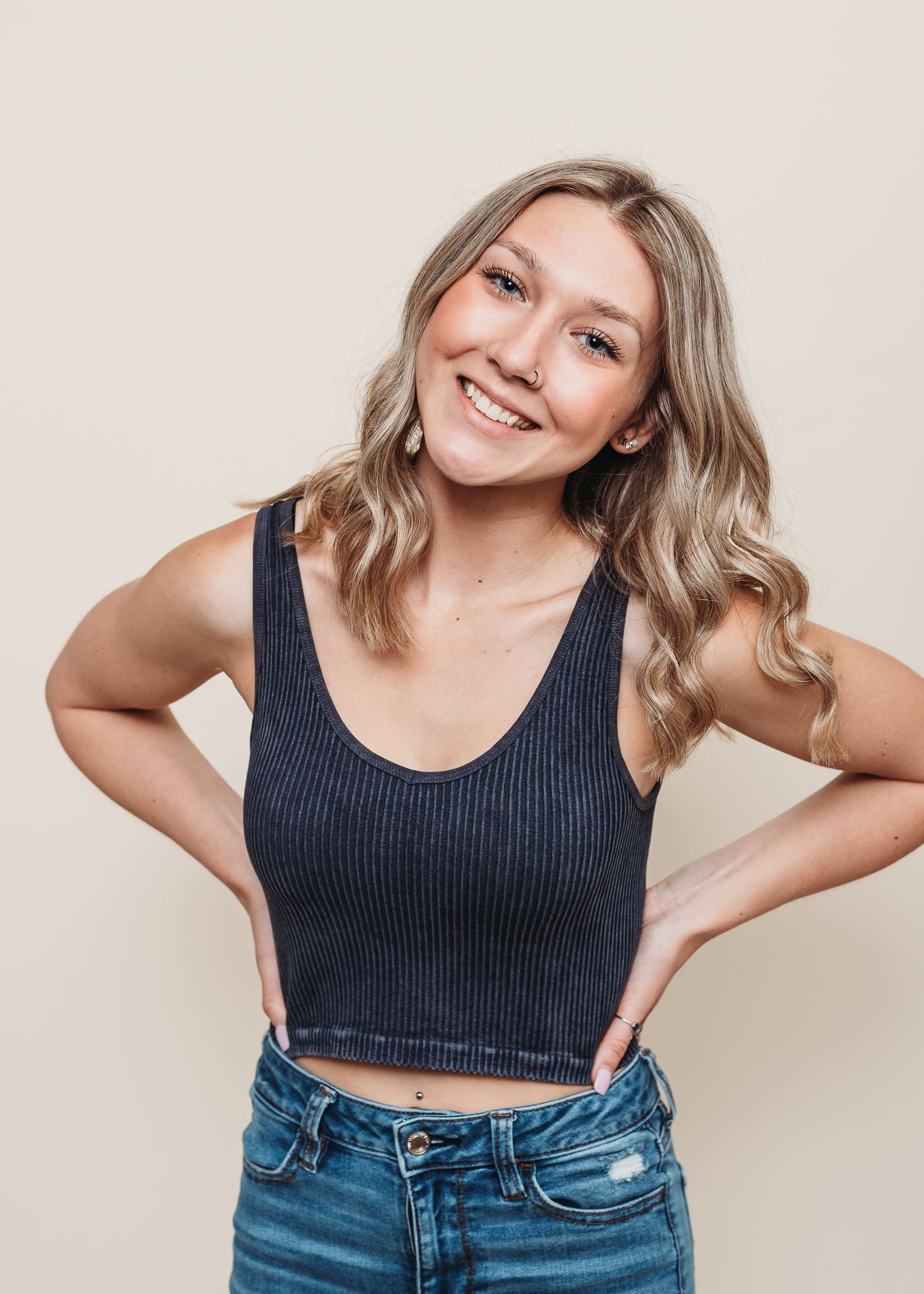 Studio portrait against beige background wearing navy crop top and denim.