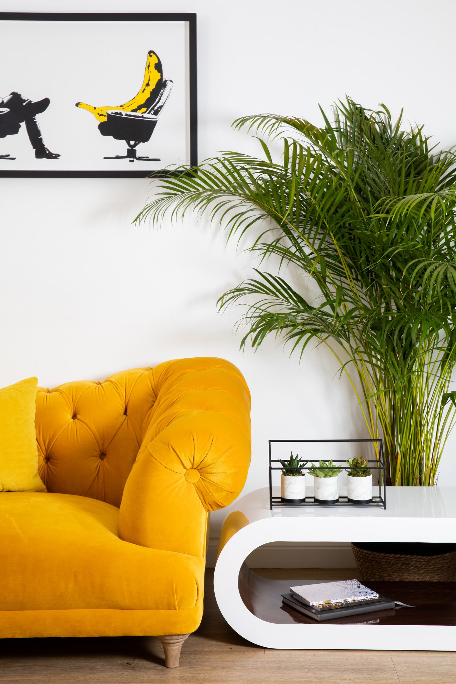 Modern interior design featuring a bright yellow tufted armchair, tropical palm plant, and minimalist artwork from a product/lifestyle photo