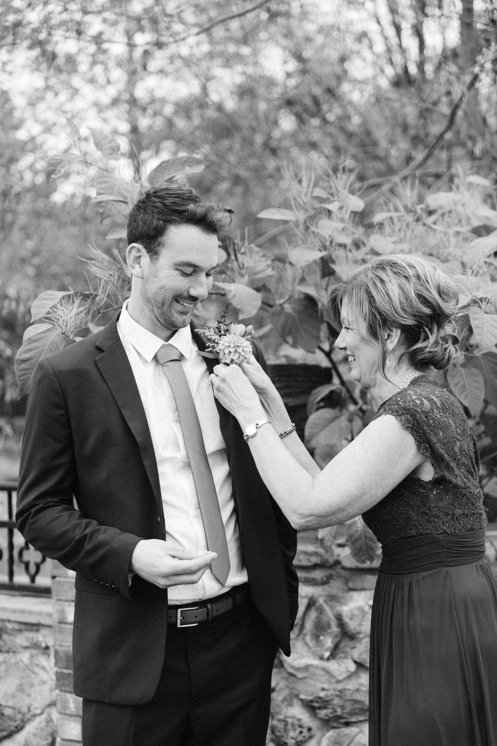 Wedding preparation moment outdoors as boutonniere is pinned on suit lapel.
