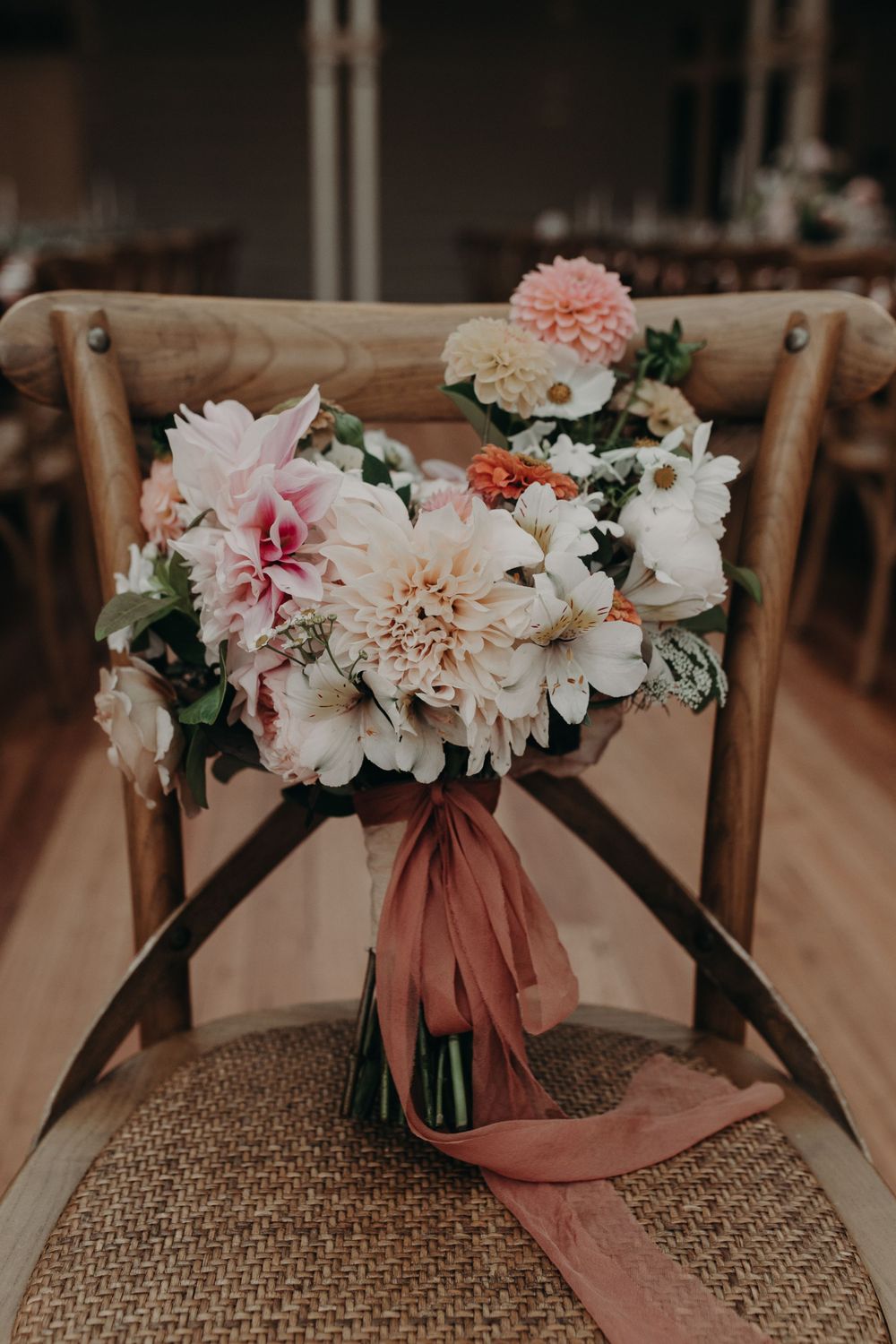 Elegant bridal bouquet with pink and white flowers tied with dusty rose ribbon on wooden chair.