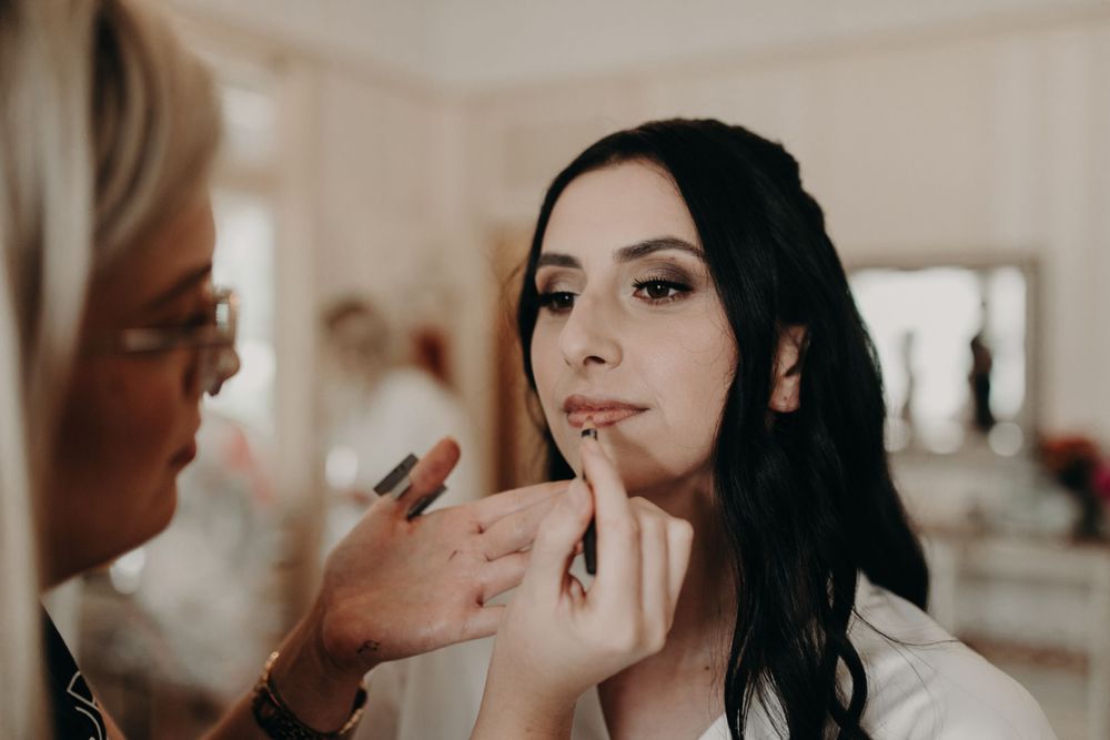 Professional makeup artist applying lipstick during bridal preparation.