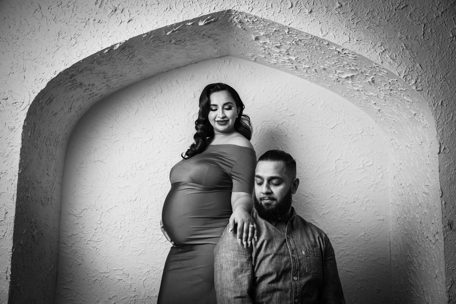 A maternity photo shoot featuring a couple in black and white under an arched doorway.