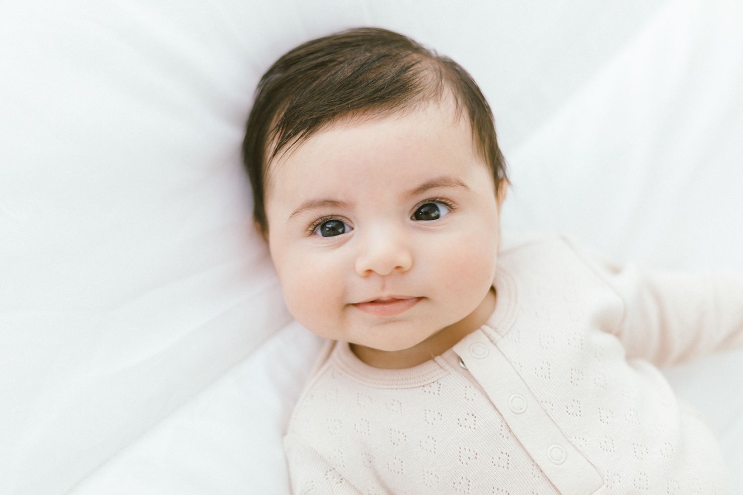 Happy baby wearing soft cream colored outfit against white background.