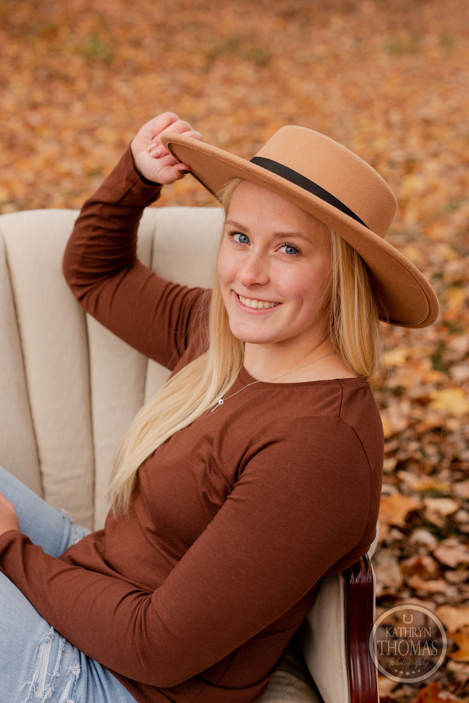 Candid autumn portrait in a beige armchair wearing brown sweater and tan wide brim hat.
