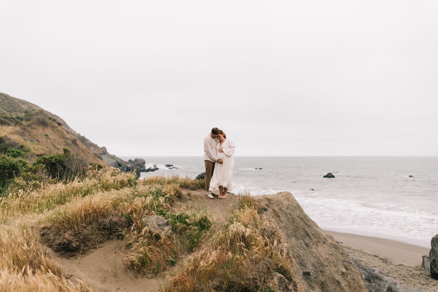 Couple embracing on a scenic coastal cliff overlooking the Pacific Ocean.