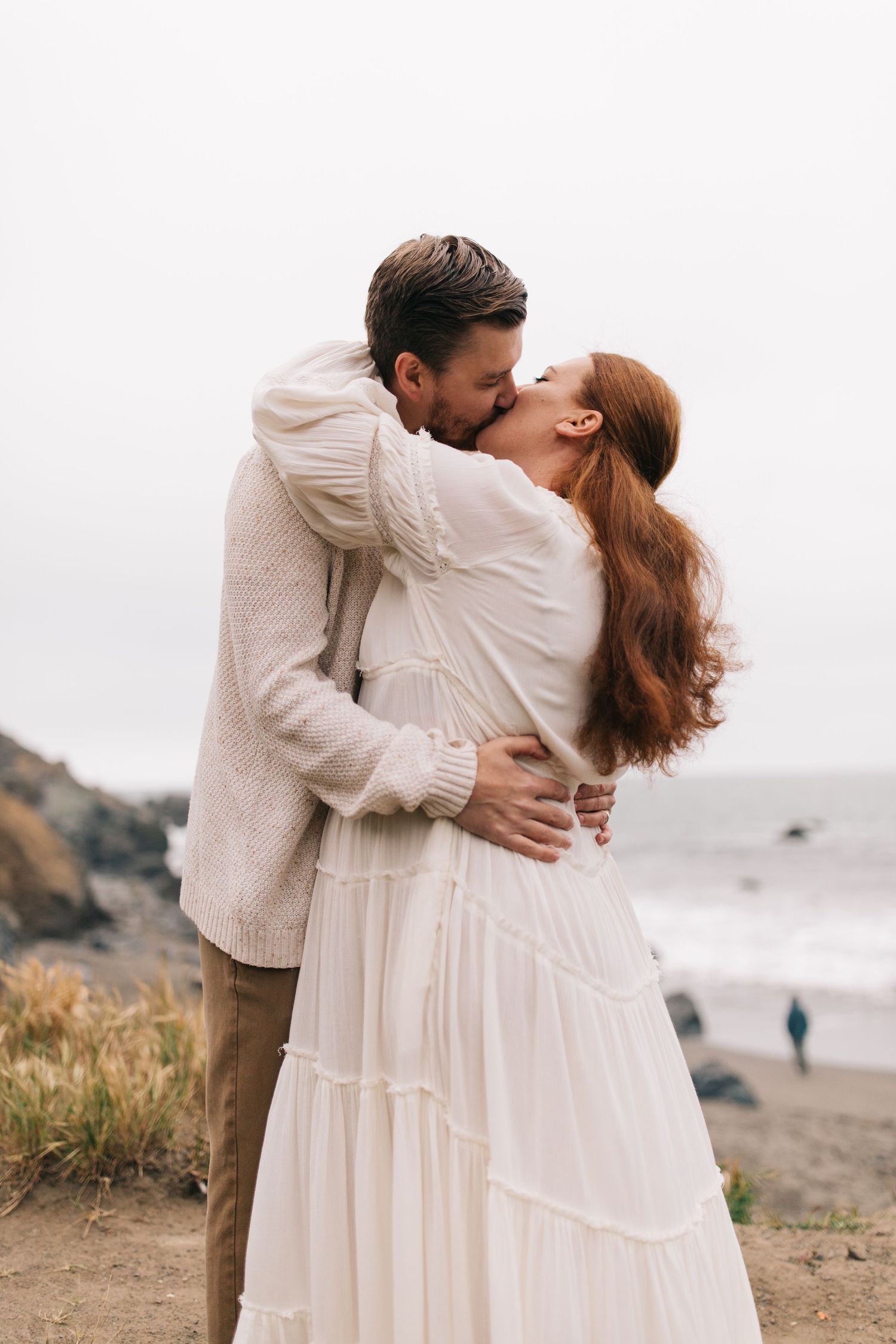 Romantic kiss captured against a misty coastal backdrop.