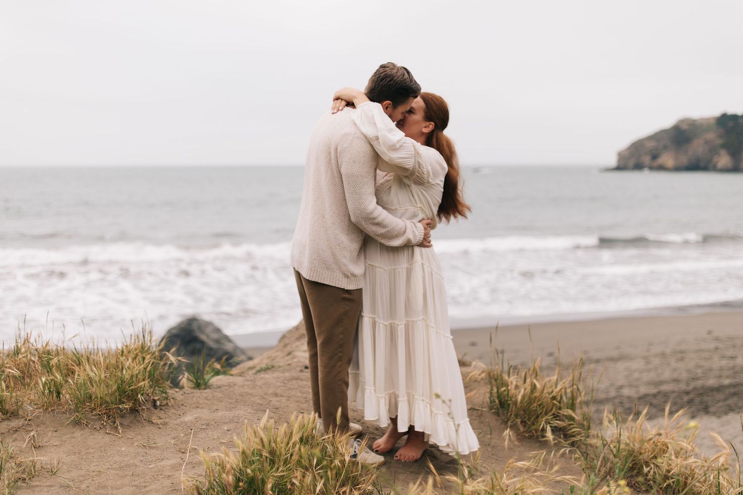 Loving embrace on a coastal path with ocean waves in the distance.