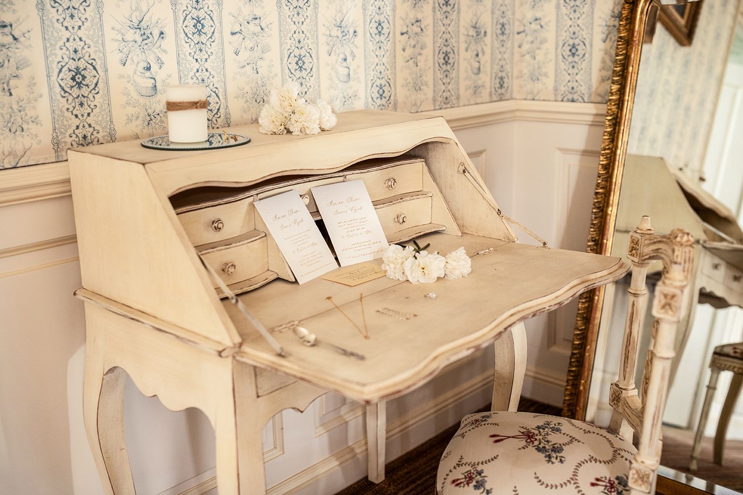 Vintage cream-colored secretary desk with ornate details in elegant French-style room.