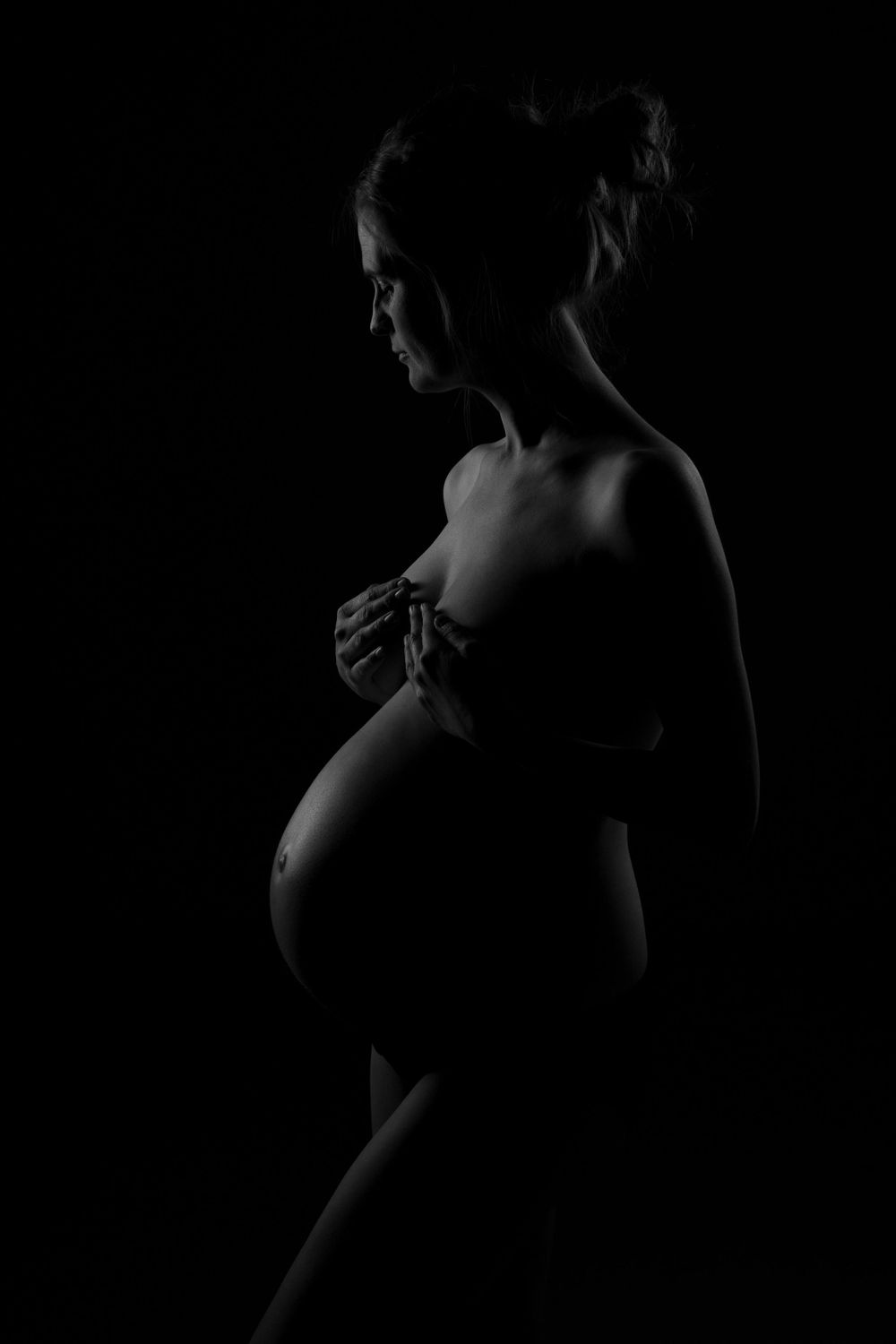 Artistic silhouette maternity photo in dark lighting.