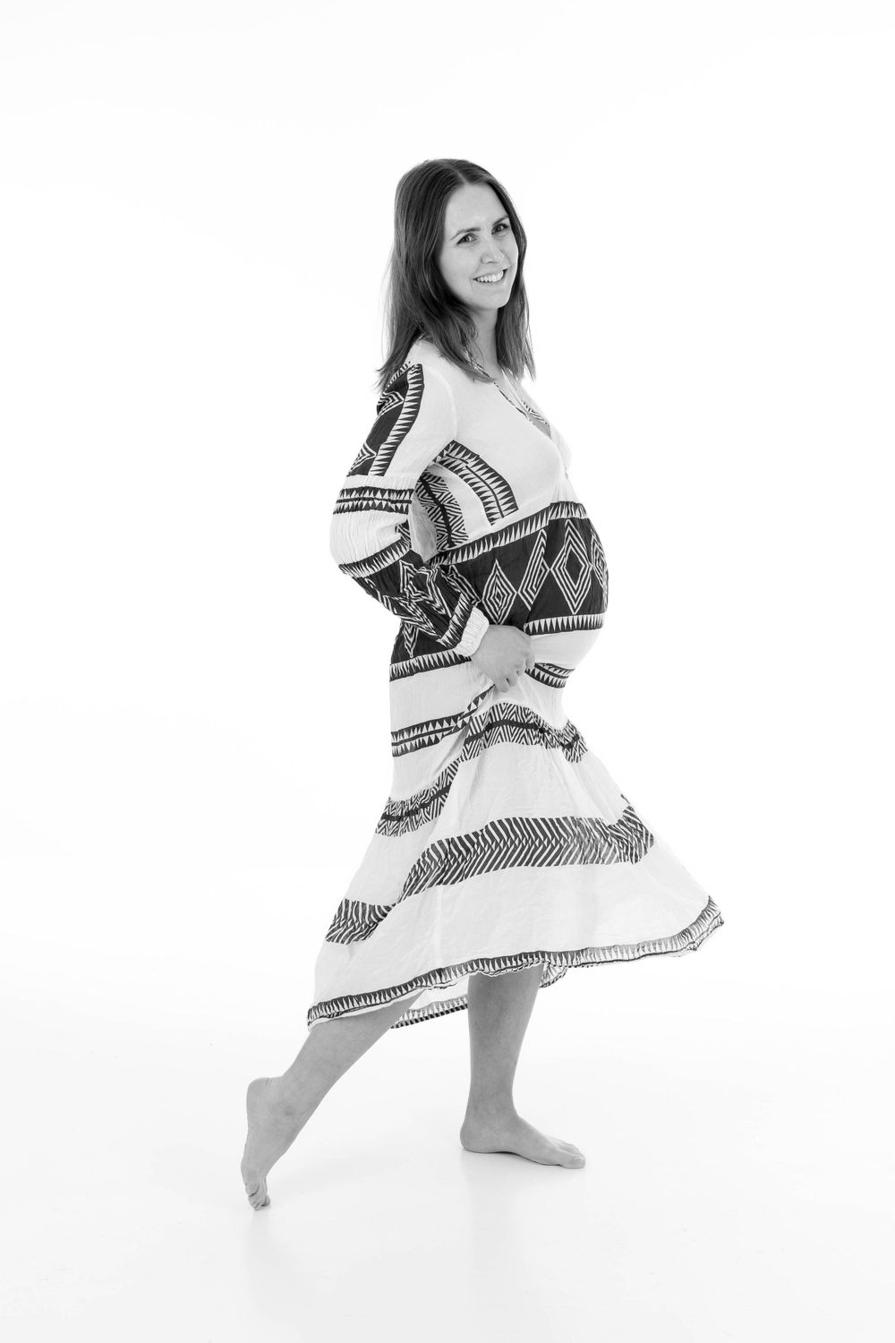 Woman in a flowing patterned dress twirling in a black and white portrait.