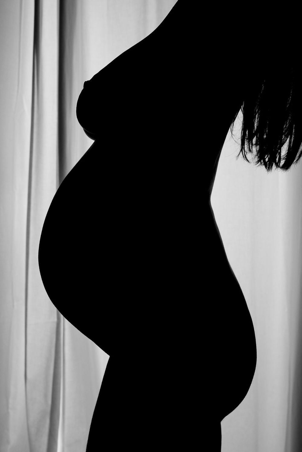 Black and white silhouette profile of a pregnant belly against a light background.