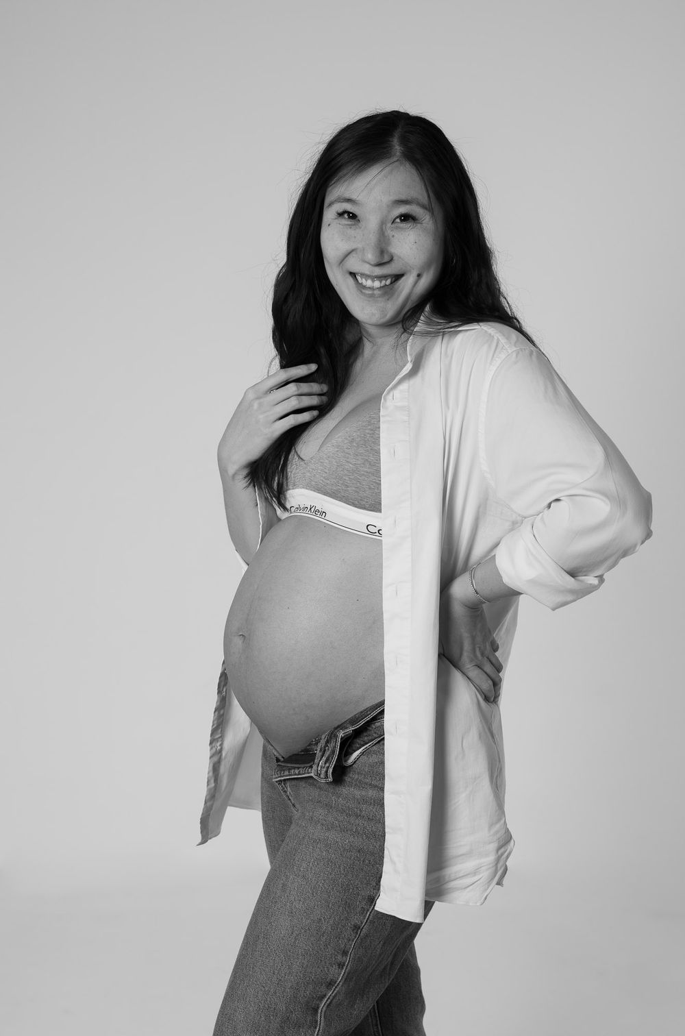 Black and white portrait of an expectant mother in casual attire smiling at the camera.