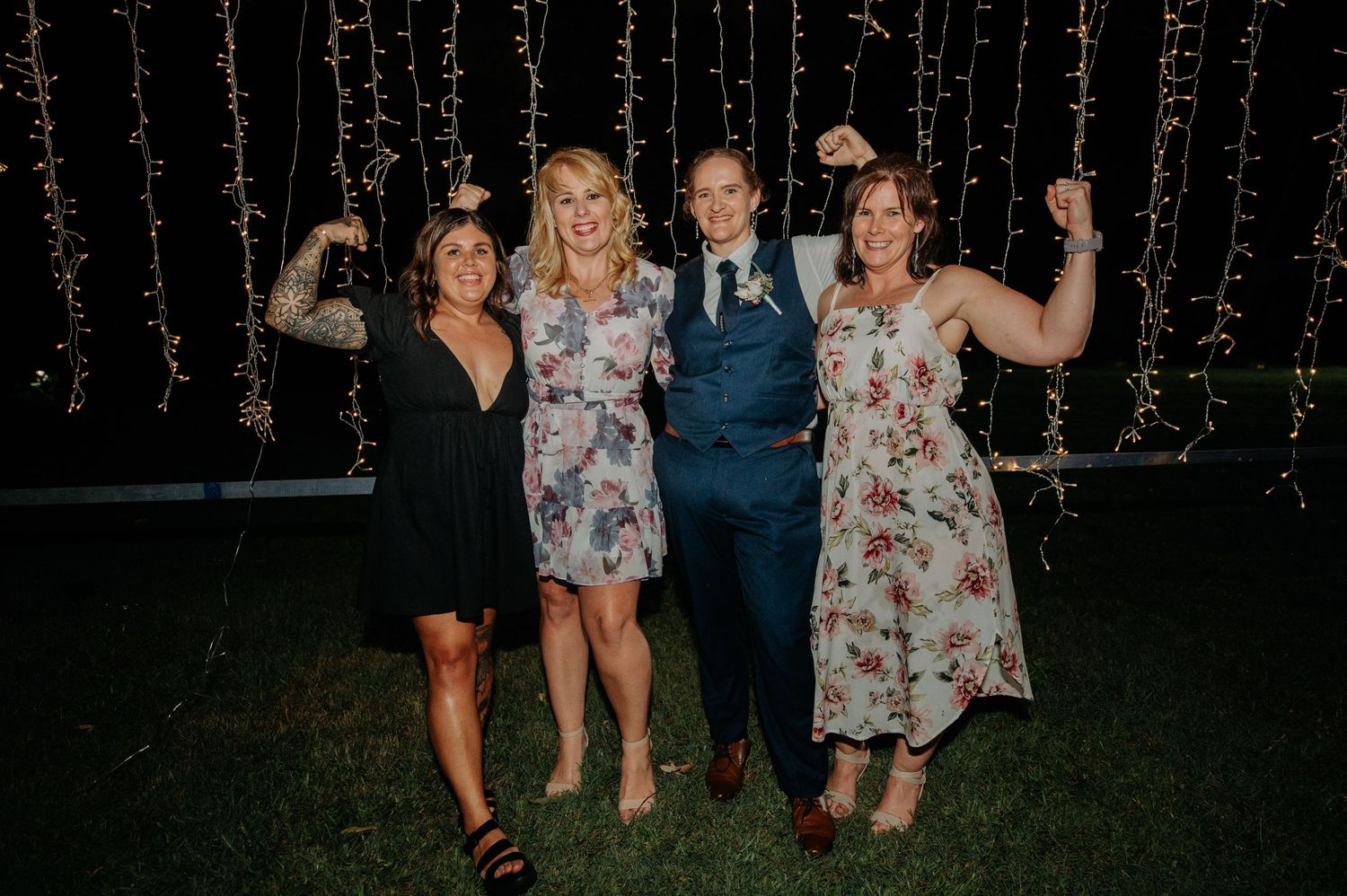 Wedding guests celebrate against backdrop of twinkling fairy lights at night.