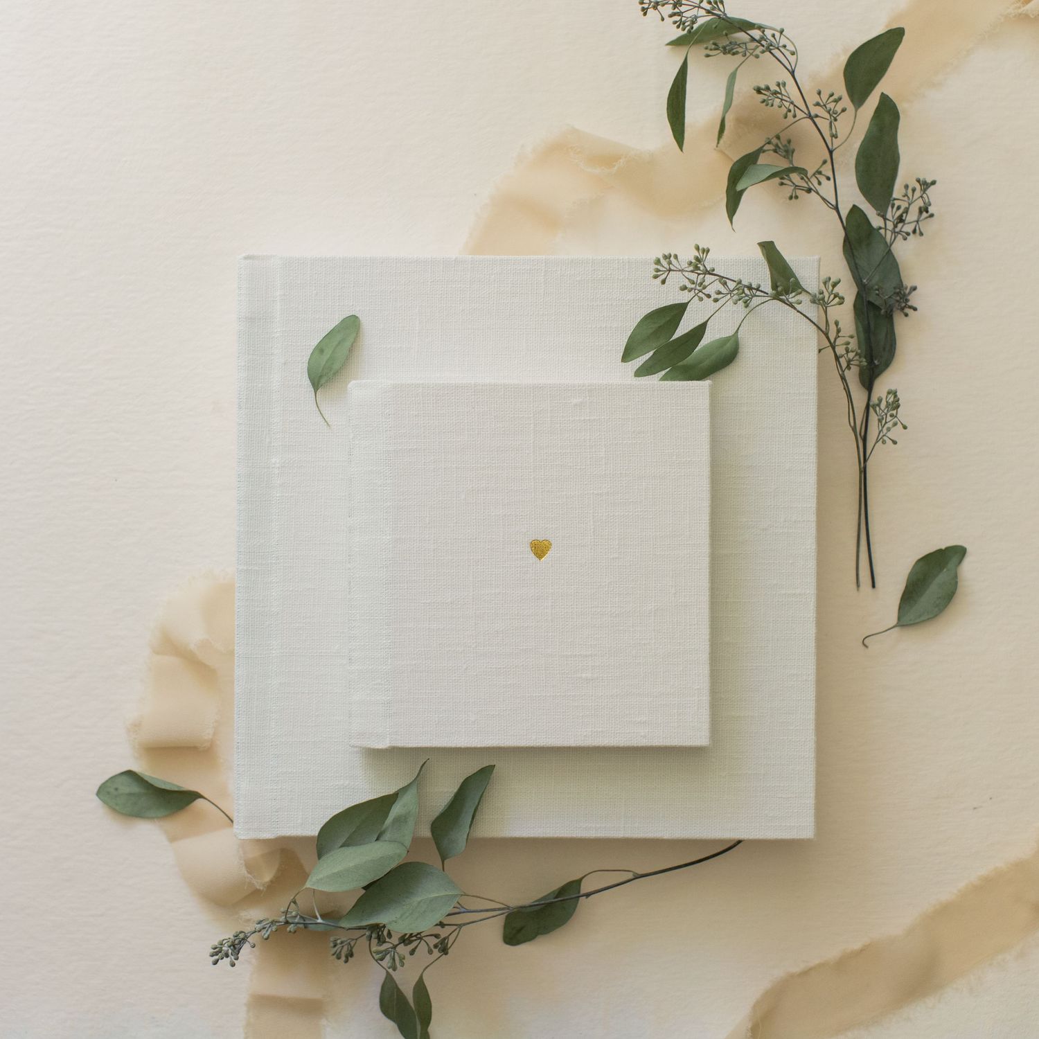 White paper cards arranged with delicate eucalyptus leaves on a cream colored background.