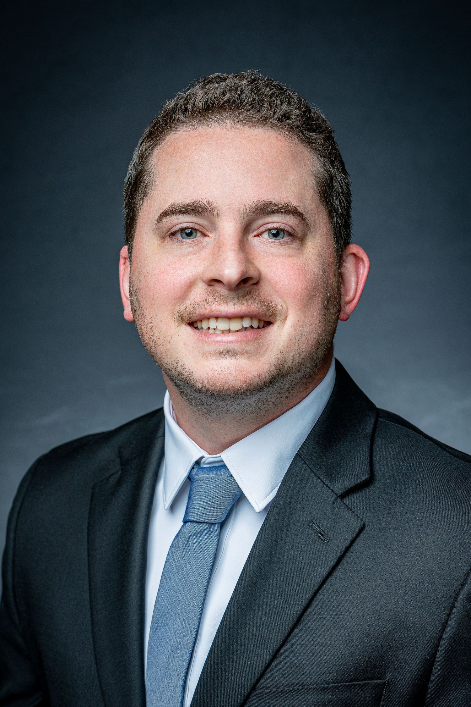 Professional headshot of suited businessman against dark background.