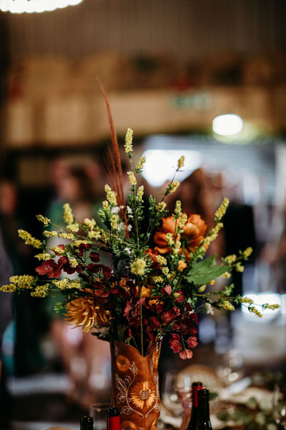 Autumn floral centerpiece with orange and yellow blooms in copper vase at wedding reception.