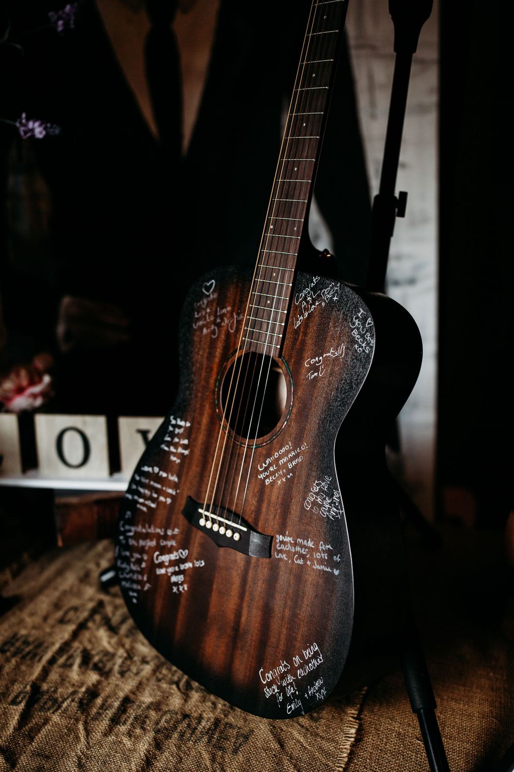 A wooden acoustic guitar with handwritten signatures and messages decorating its surface rests on a rustic wooden surface.