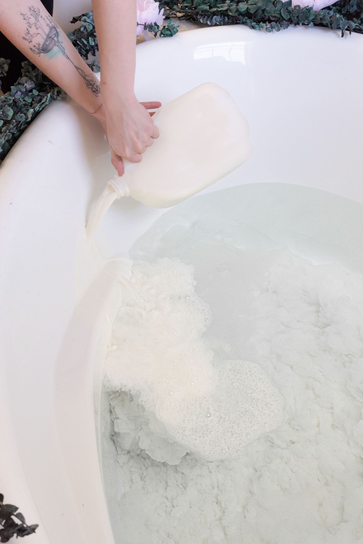 Adding milk bath mixture to white bathtub with visible tattooed arm.