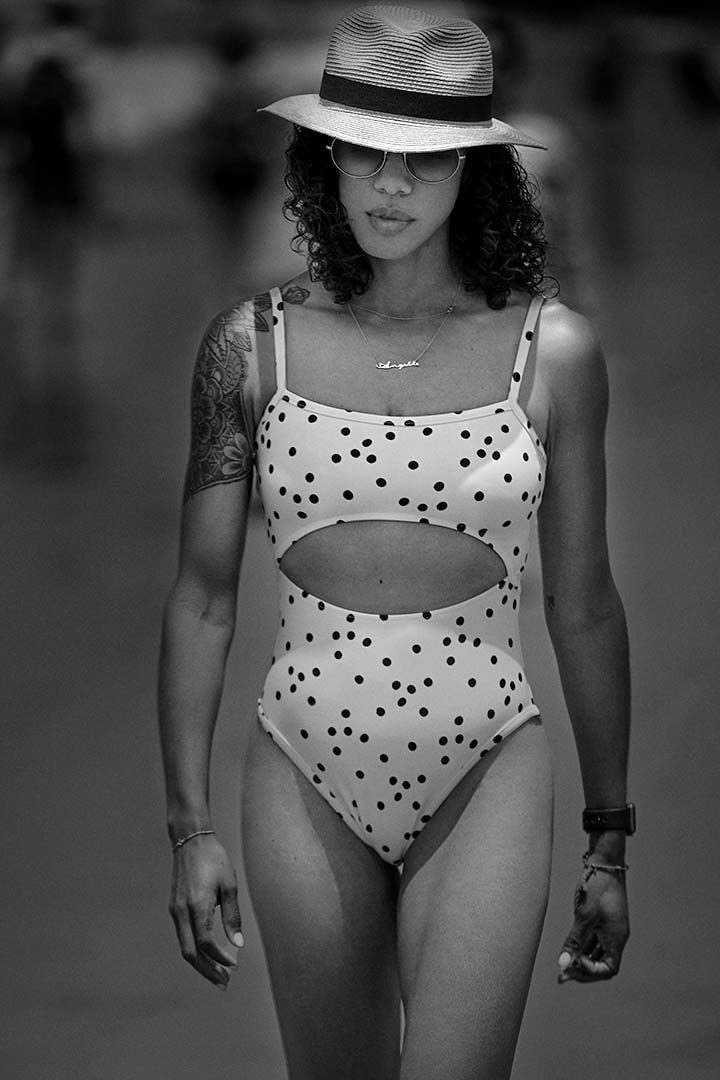 Black and white photo of a model in a polka dot swimsuit and fedora hat posing elegantly.