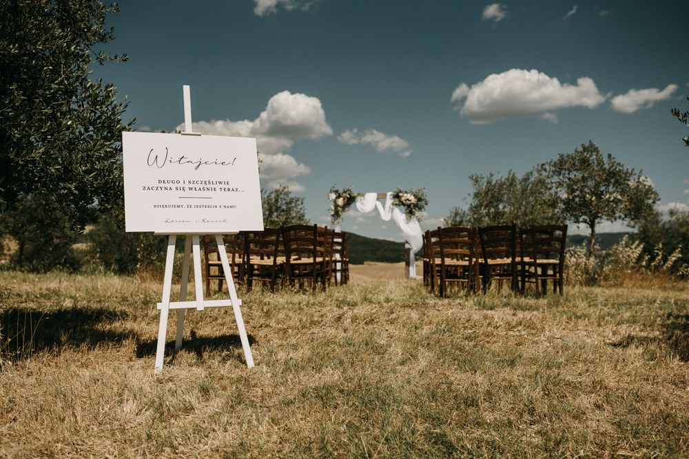 Rustic outdoor wedding welcome sign display against a golden field with white easels and greenery.