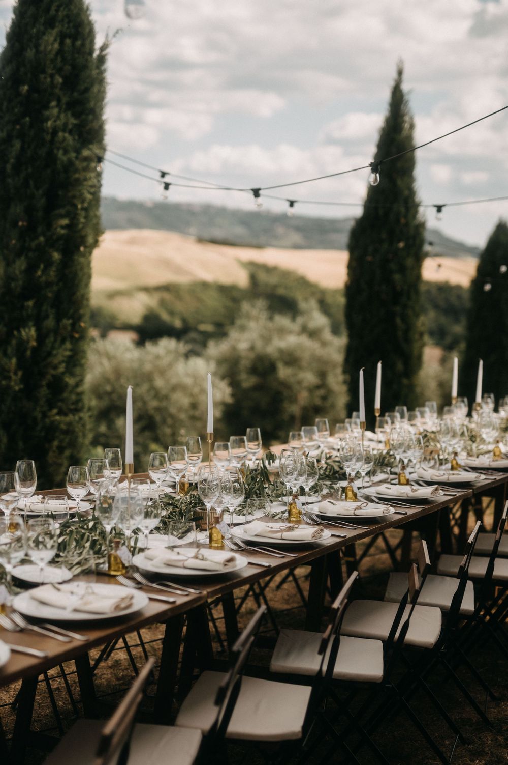 Elegant outdoor wedding reception table settings with string lights and cypress trees in Tuscany.