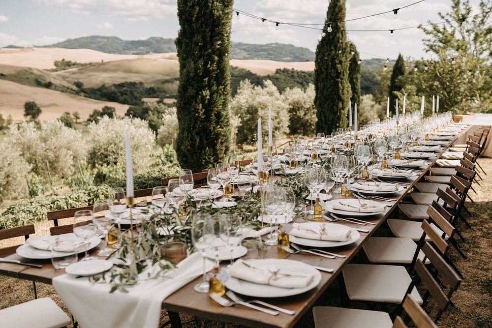 Outdoor wedding reception tables with white place settings and natural decor against Tuscan landscape.