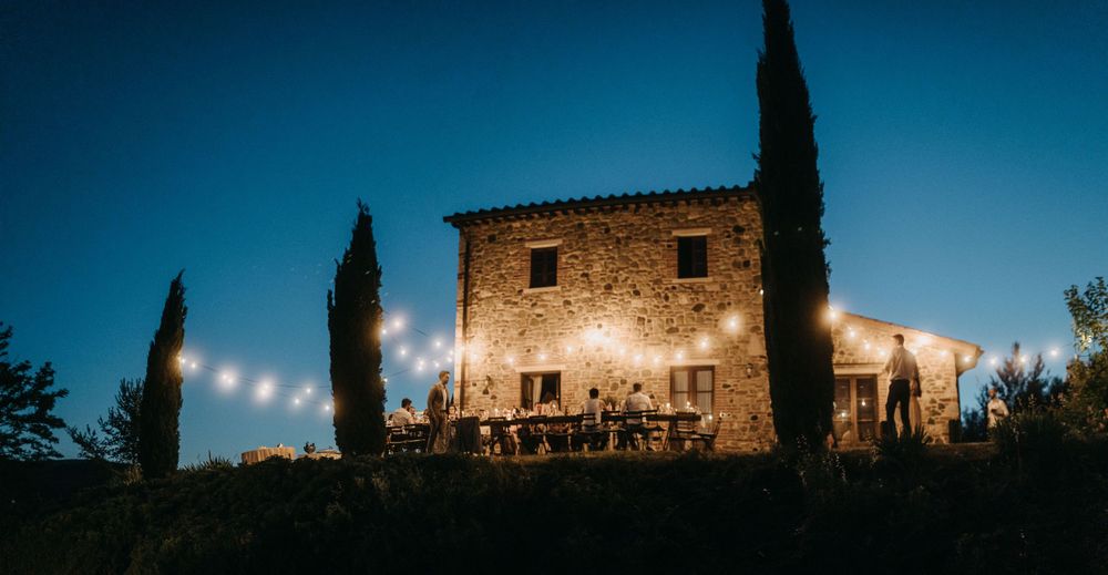 Dramatic blue hour silhouette of Italian villa and cypress trees against evening sky.
