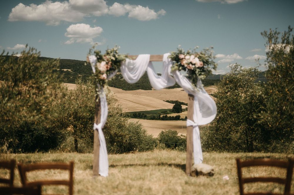 Wedding ceremony site in a sun-filled meadow with white draped arch and wooden chairs.