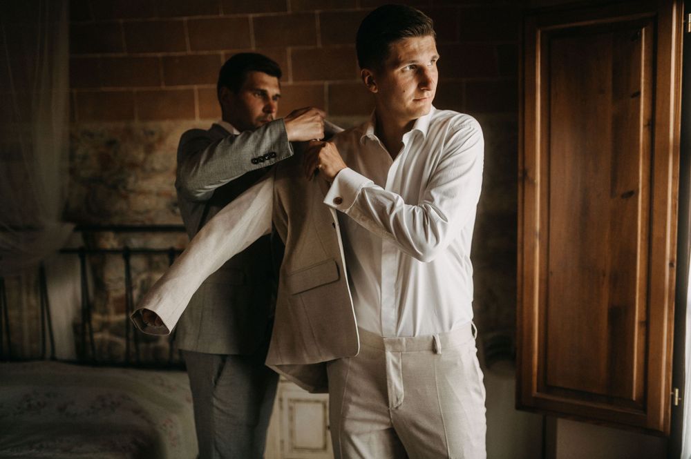 Two people getting dressed in formal attire in an elegant rustic room with stone walls.
