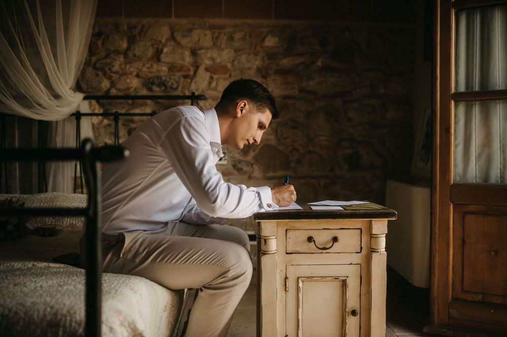 Person writing at an antique wooden desk next to a stone wall.