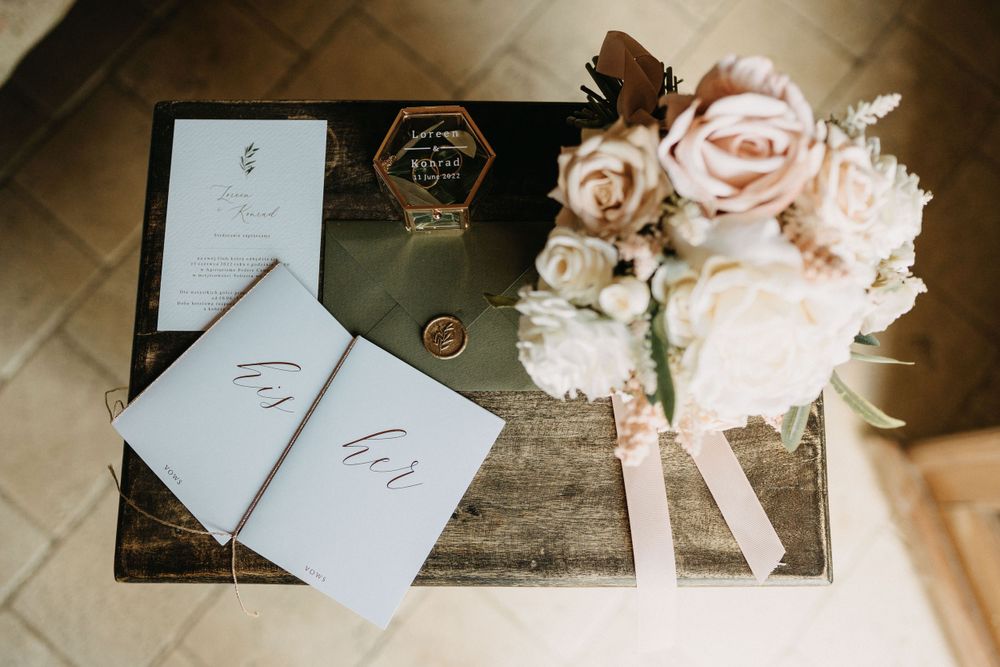Wedding stationery set with white invitations and pink roses on wooden surface.
