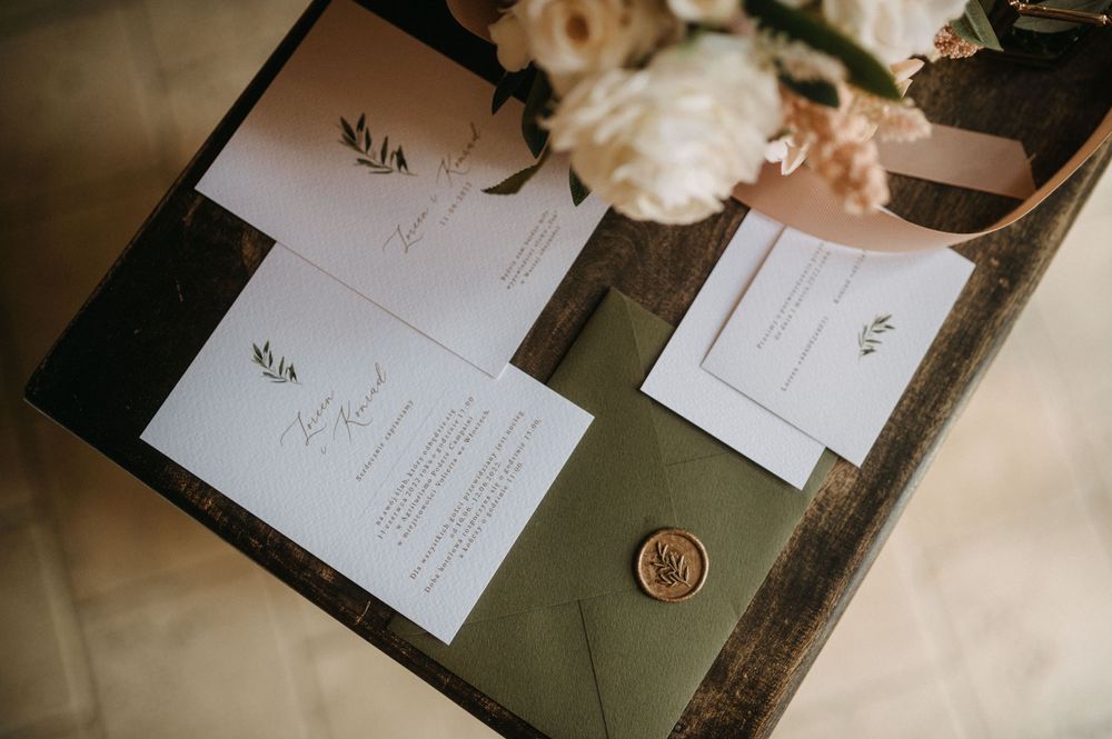 Wedding invitation suite with elegant white stationery and wax seal on dark green surface.