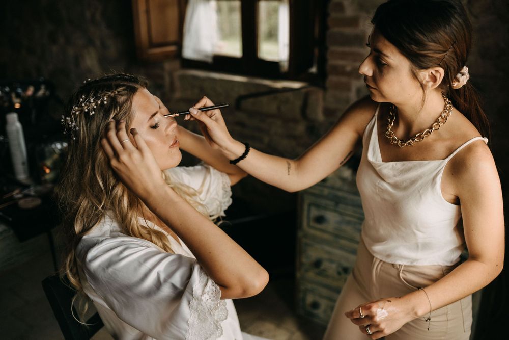 Wedding makeup application in progress in rustic stone-walled room.