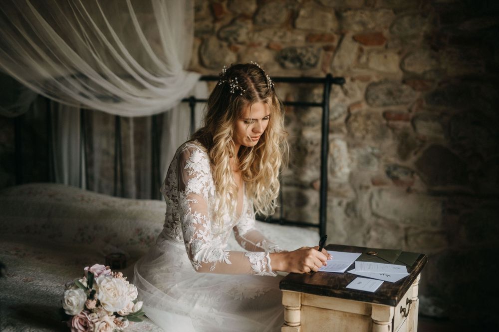 Bride signing documents at rustic wooden desk in stone-walled room.