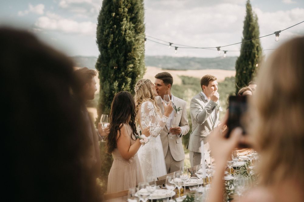 Wedding couple celebrating with guests at an elegant outdoor reception with cypress trees.