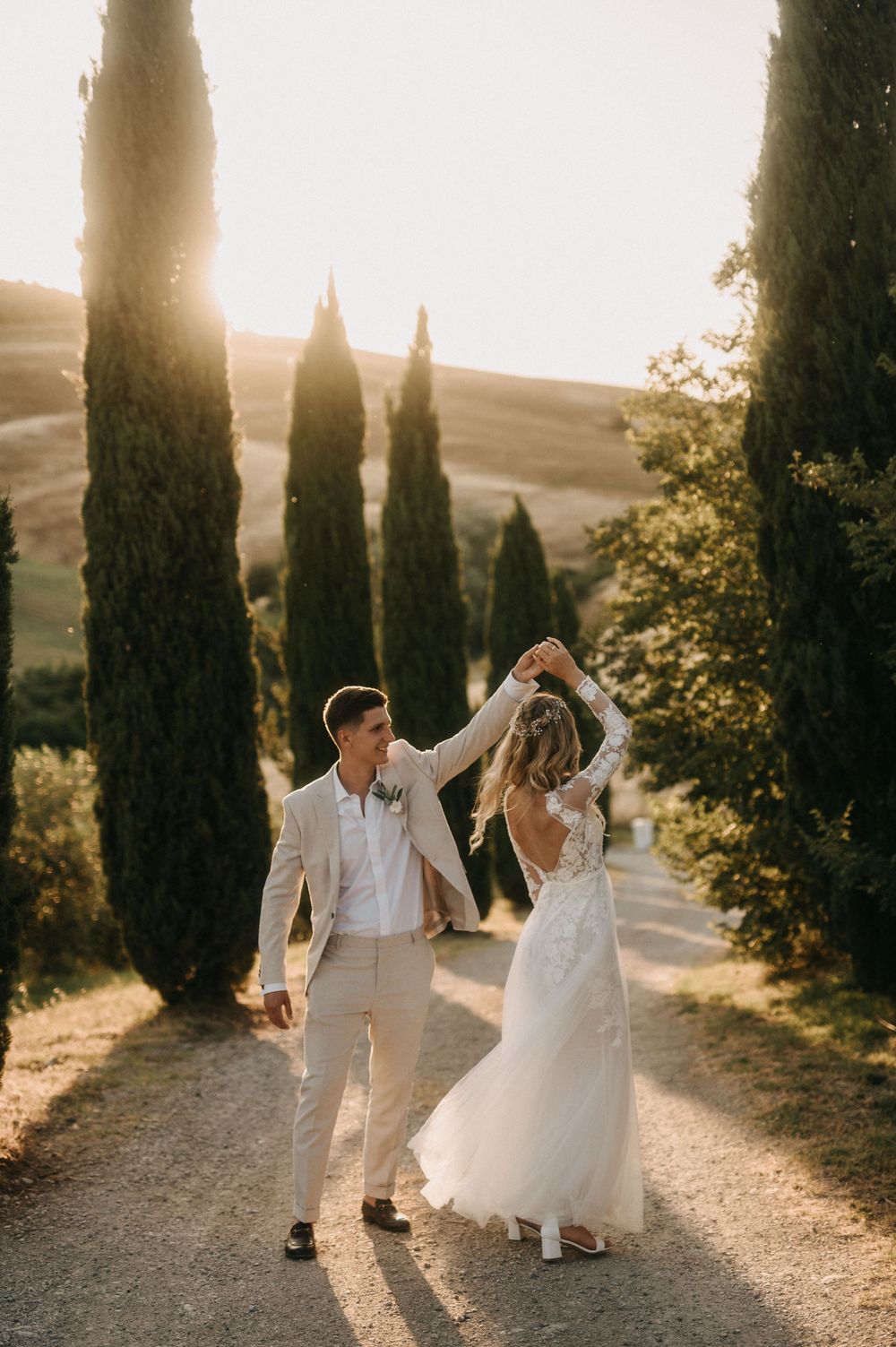 Newlyweds dancing along cypress-lined path during golden hour in Tuscany.