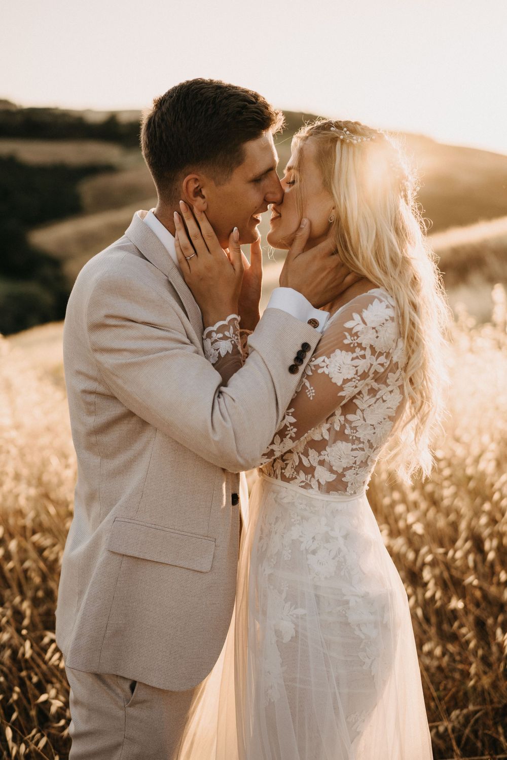 Romantic sunset portrait of bride and groom sharing intimate moment in golden field.
