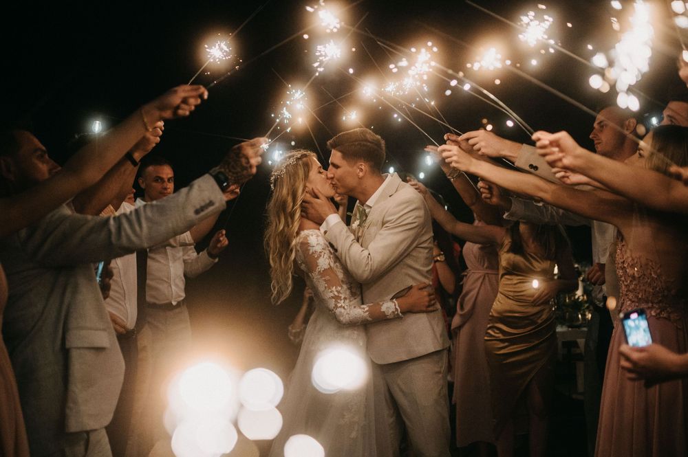 Wedding guests hold sparklers creating a magical tunnel of light during an evening celebration.