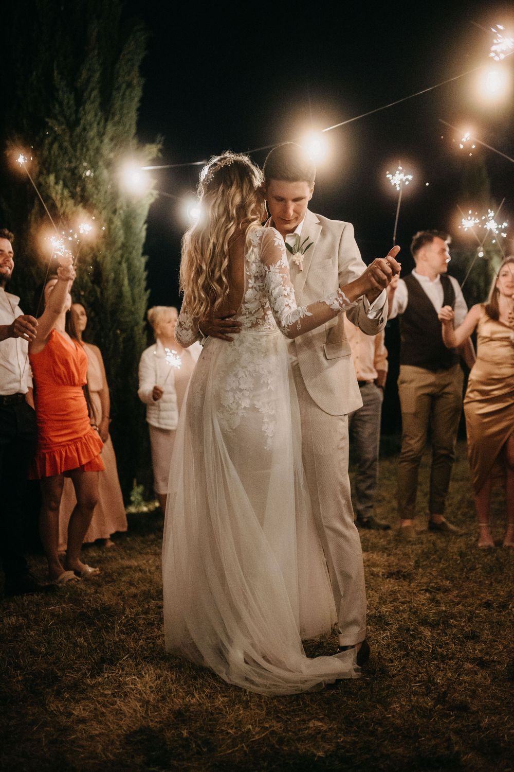Wedding celebration at night with guests holding sparklers in an outdoor setting.
