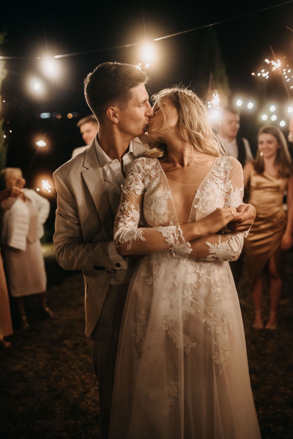 Intimate moment between newlyweds surrounded by sparklers and guests at nighttime reception.