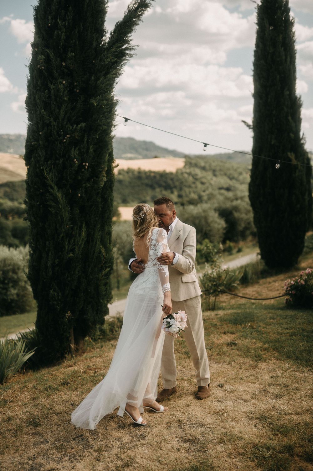 Newlyweds embrace among tall cypress trees in a romantic Tuscan landscape.