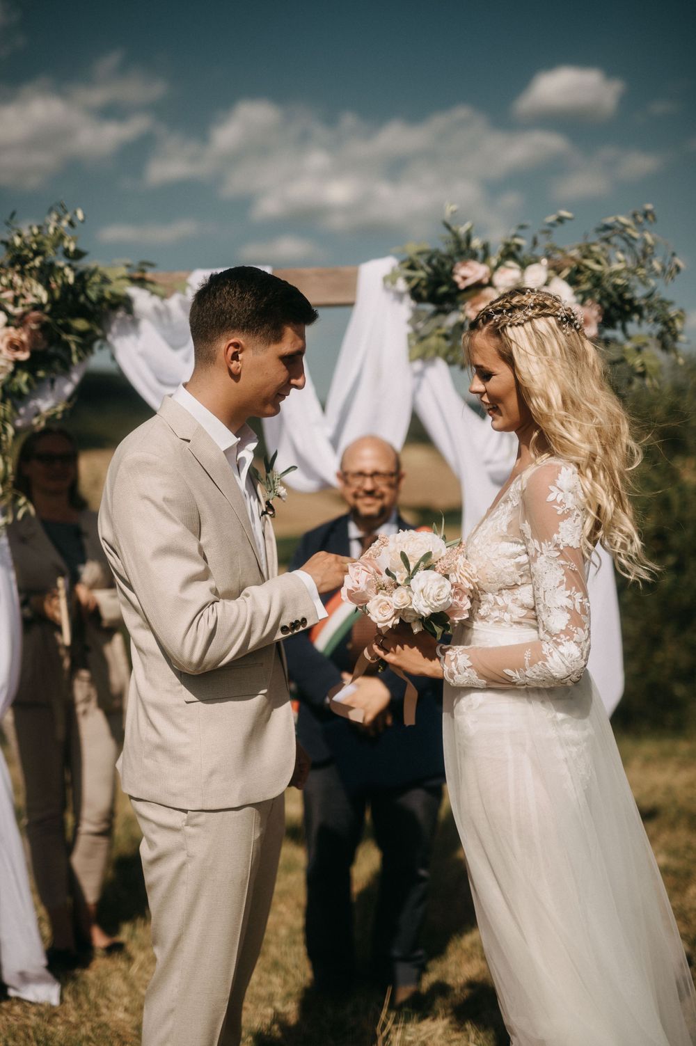 A couple exchanges rings during their intimate outdoor wedding ceremony under a floral arch.