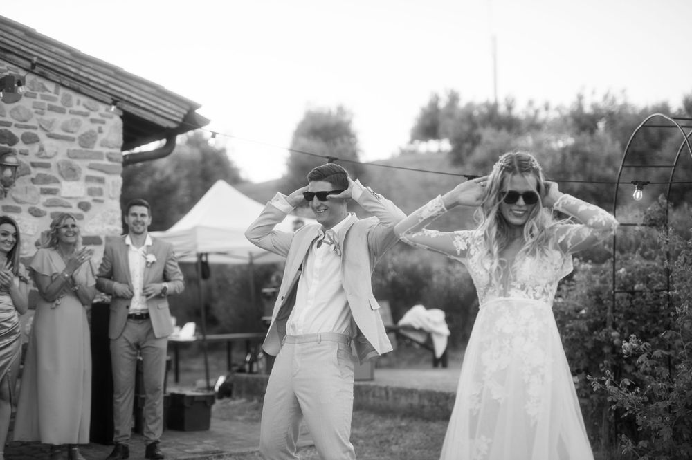 Black and white photo of newlyweds dancing with wedding guests in garden setting.