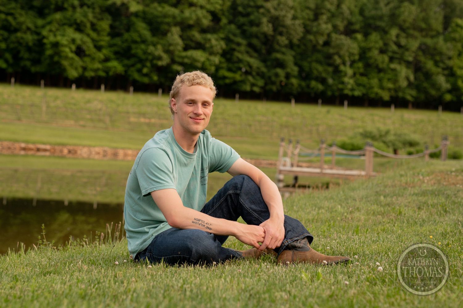 Person relaxes on grassy slope beside scenic pond on sunny day.