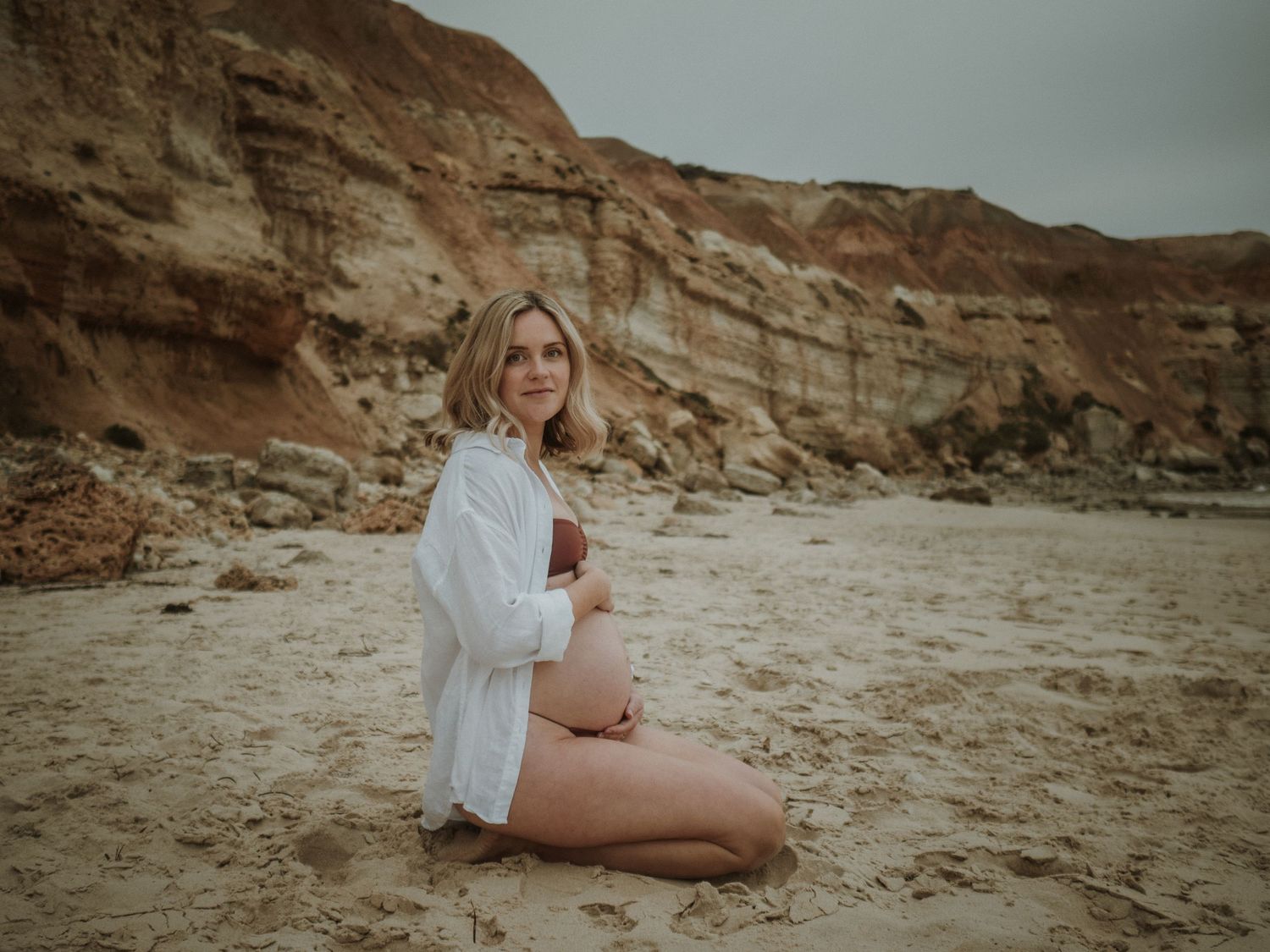 A coastal photoshoot featuring white clothing against dramatic red rock cliffs.