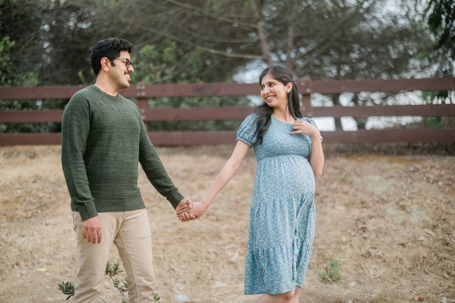 Couple shares romantic moment while holding hands against rustic wooden fence background.